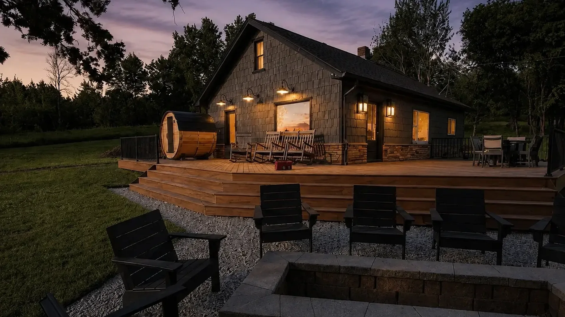 The ranch house at dusk with lit deck, cedar sauna and firepit seating